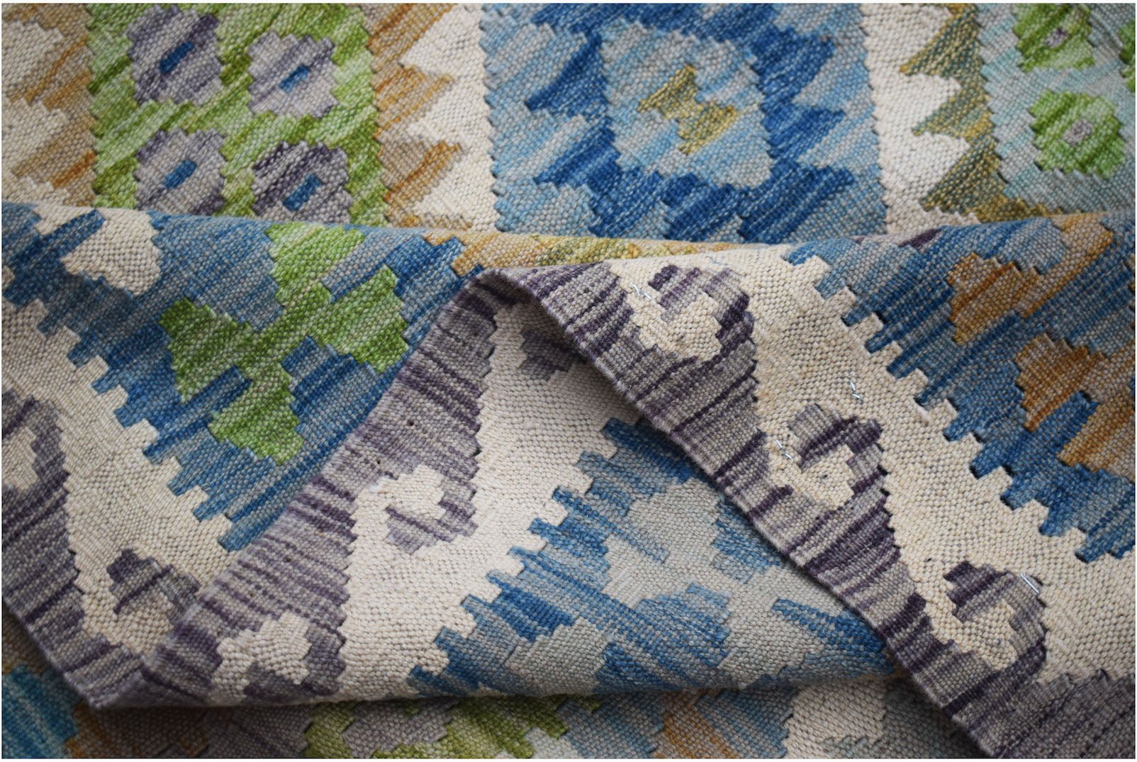 A handmade Afghan Maimana kilim rug featuring a geometric pattern in blue, green, and grey wool.