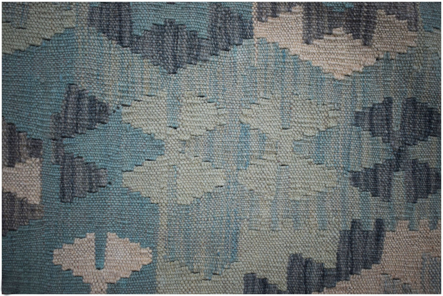 A close-up of a handmade Afghan Maimana kilim featuring a geometric pattern in blue and cream wool.
