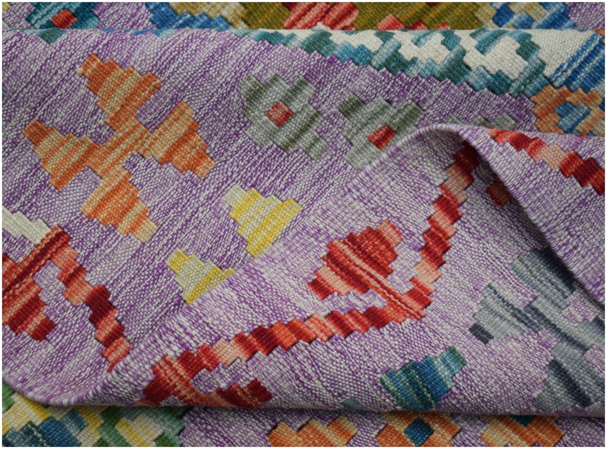A handwoven Afghan Maimana kilim rug featuring a vibrant geometric pattern on a purple background.