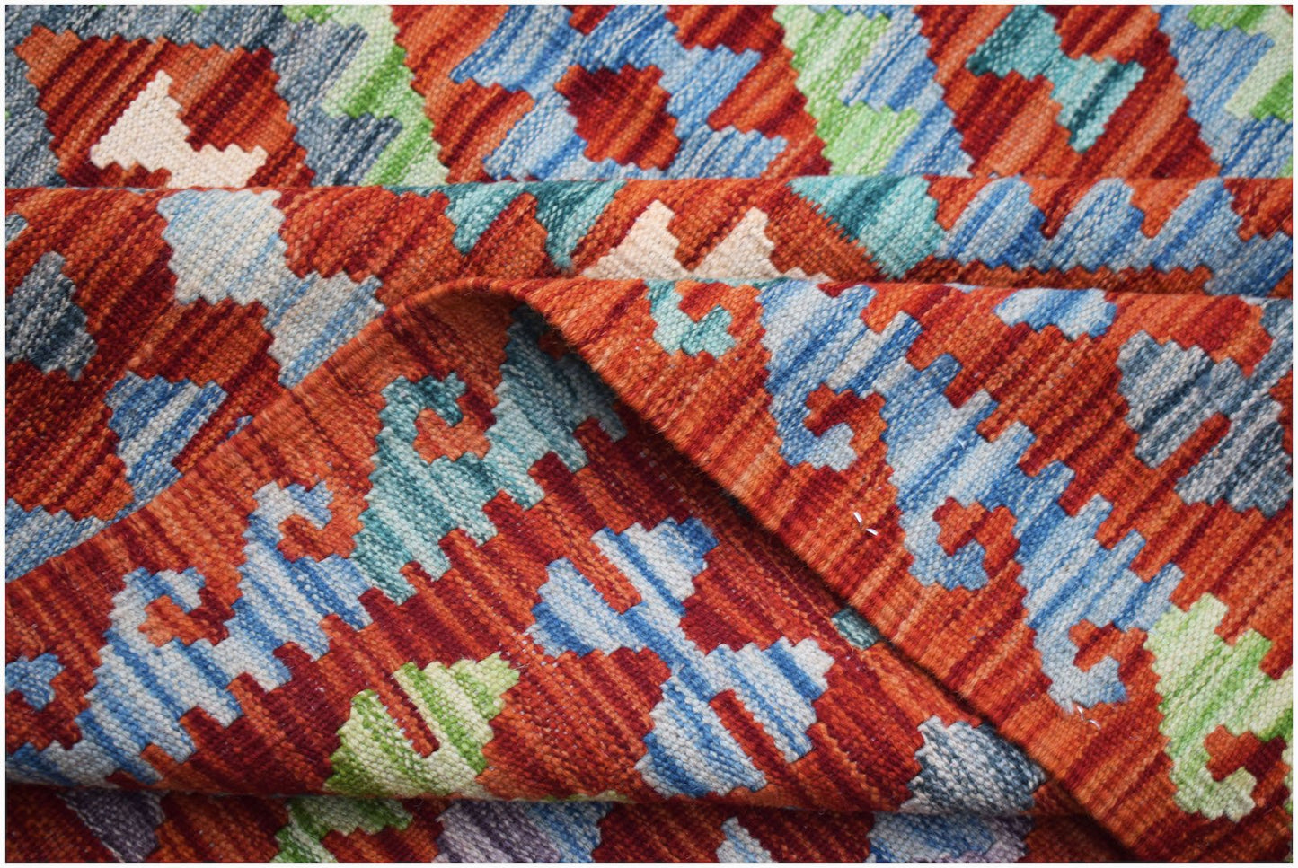 A handwoven Afghan Maimana kilim rug featuring a geometric pattern in red, blue, and green wool.