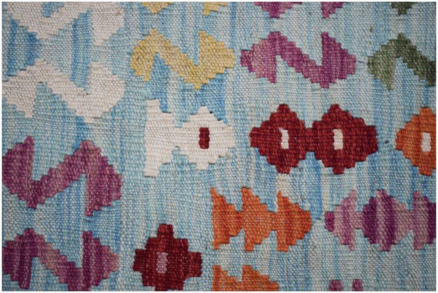 A close-up of a handmade Afghan Maimana Kilim featuring colorful geometric patterns on a blue base.