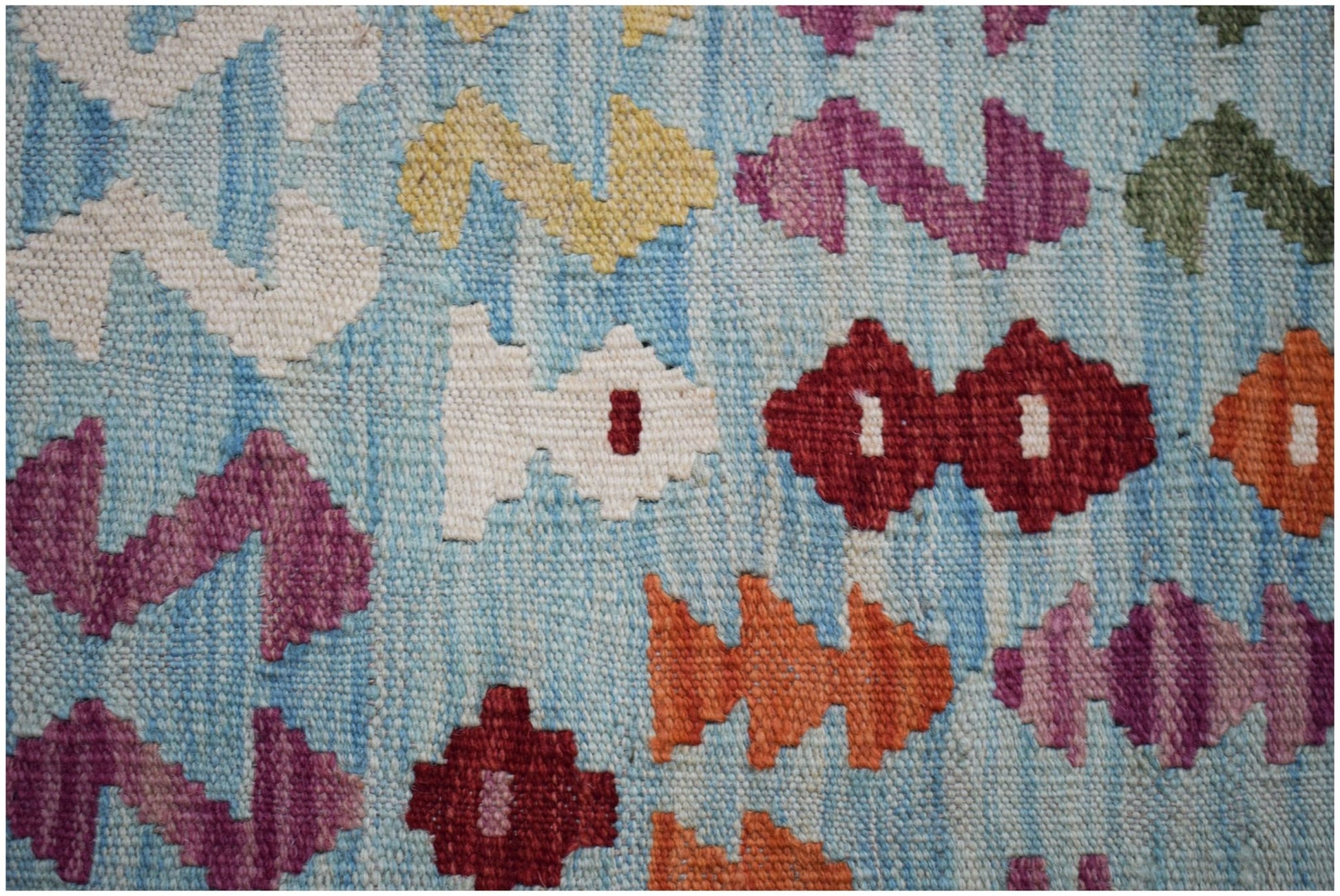 A close-up of a handmade Afghan Maimana Kilim featuring colorful geometric patterns on a blue base.
