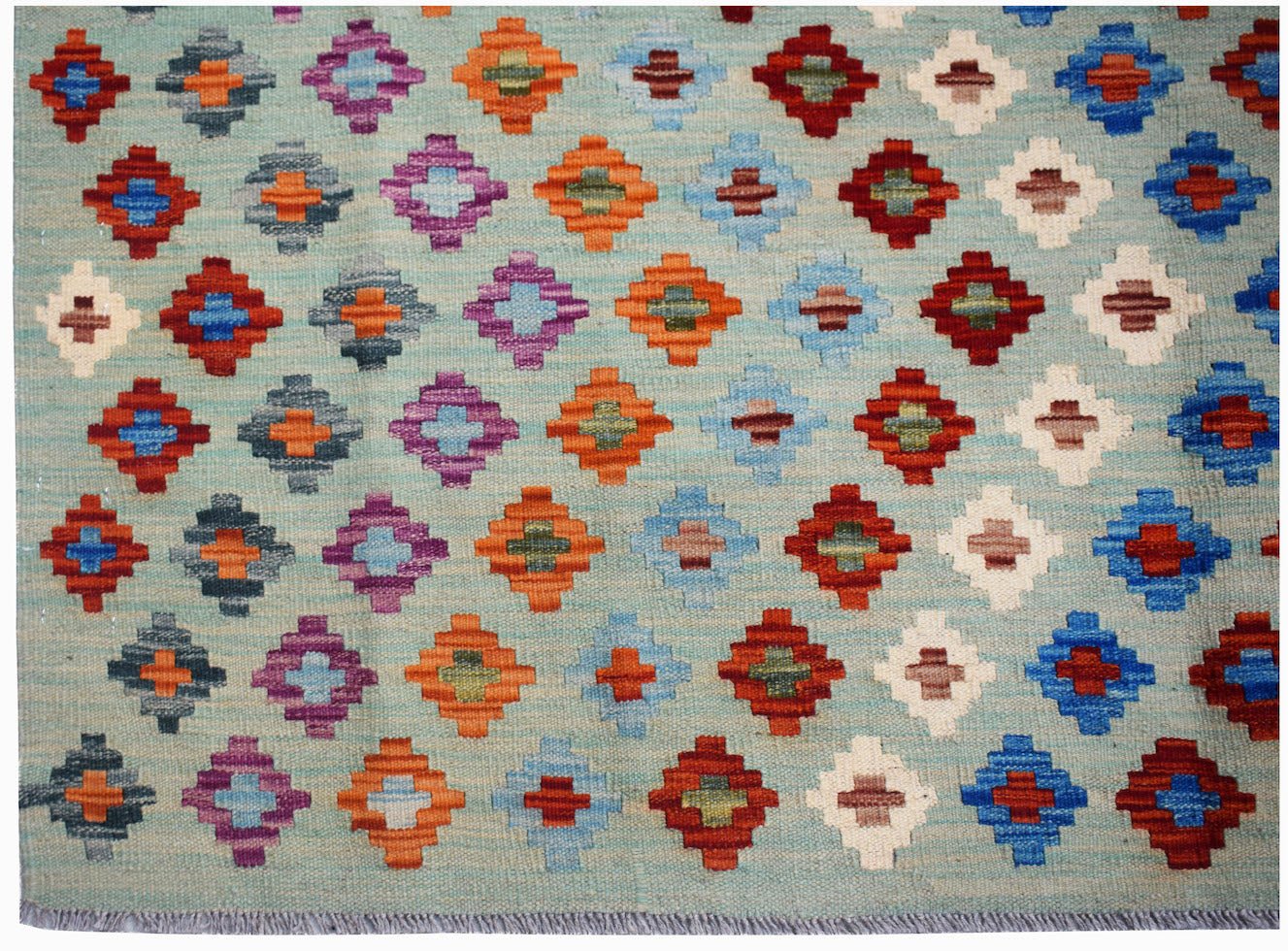 Afghan Maimana Kilim with geometric diamond patterns in various colors on a light blue background.