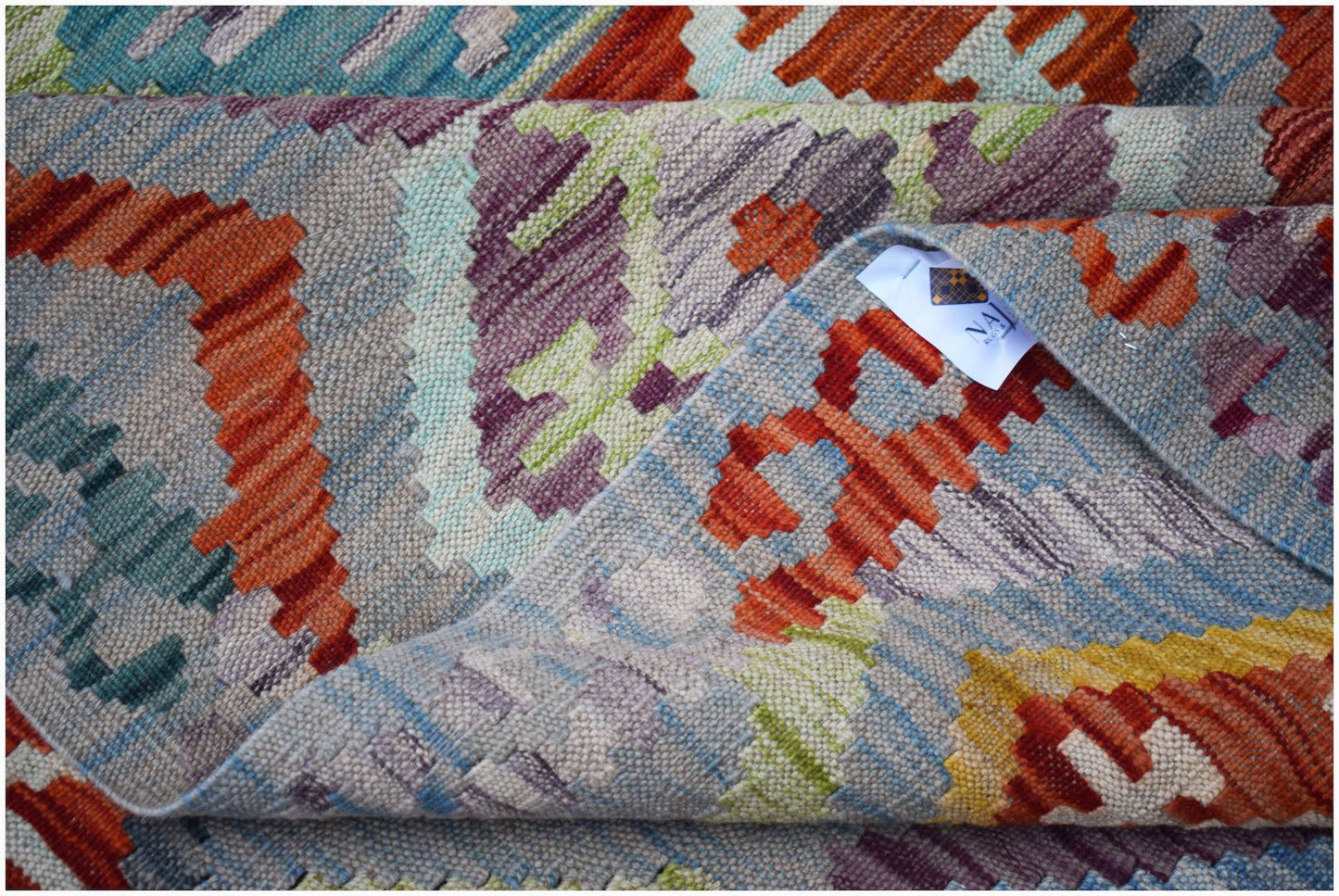 A handwoven Afghan Maimana kilim rug featuring a colorful geometric pattern in wool.