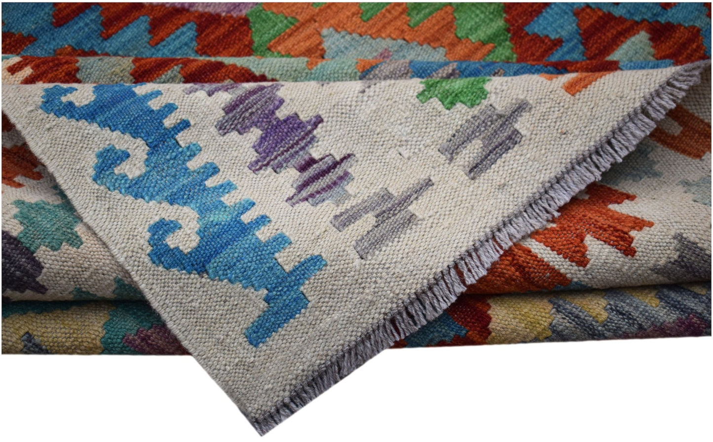 A folded Afghan Maimana kilim rug featuring vibrant geometric patterns in wool.