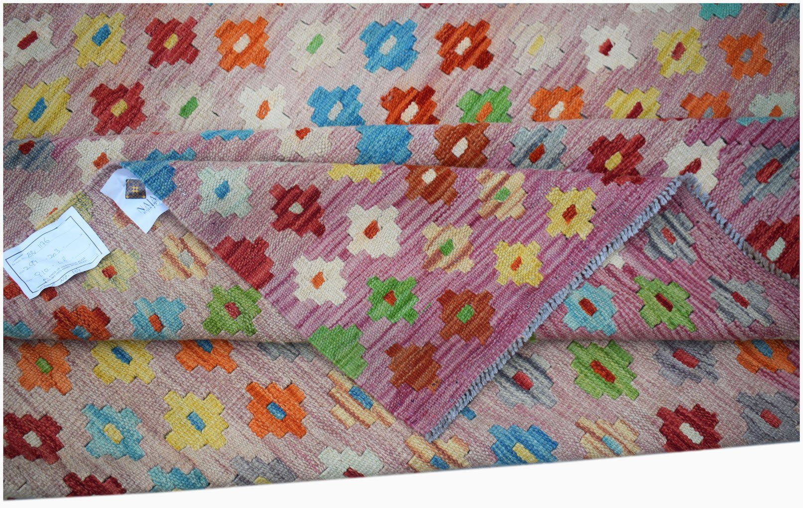 A handmade Afghan Maimana kilim featuring a pink background with colorful geometric motifs.