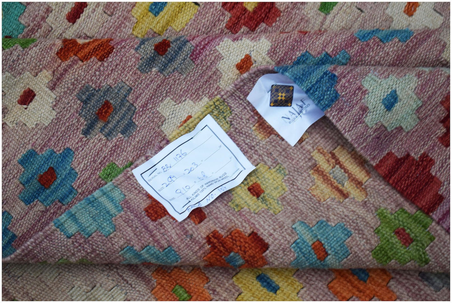 A handmade Afghan Maimana kilim featuring a geometric pattern in vibrant colors on a pink background.