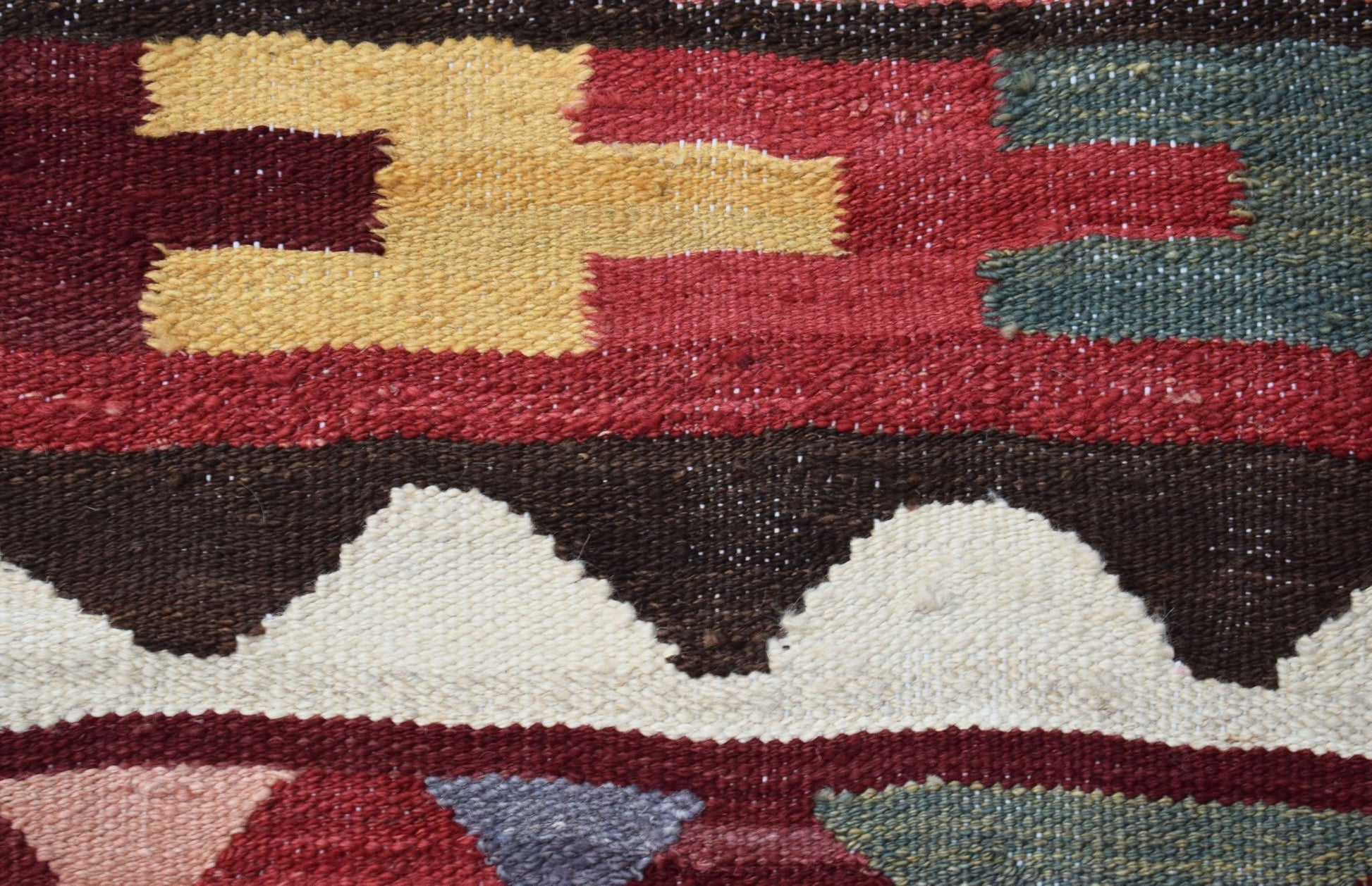 A close-up of a handmade Afghan Maimana kilim featuring geometric patterns in red, yellow, and white.