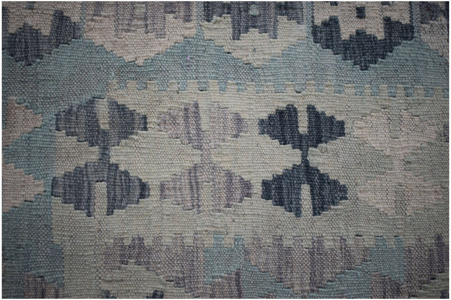 A close-up of a handmade Afghan Maimana kilim featuring a geometric pattern in blue and grey tones.