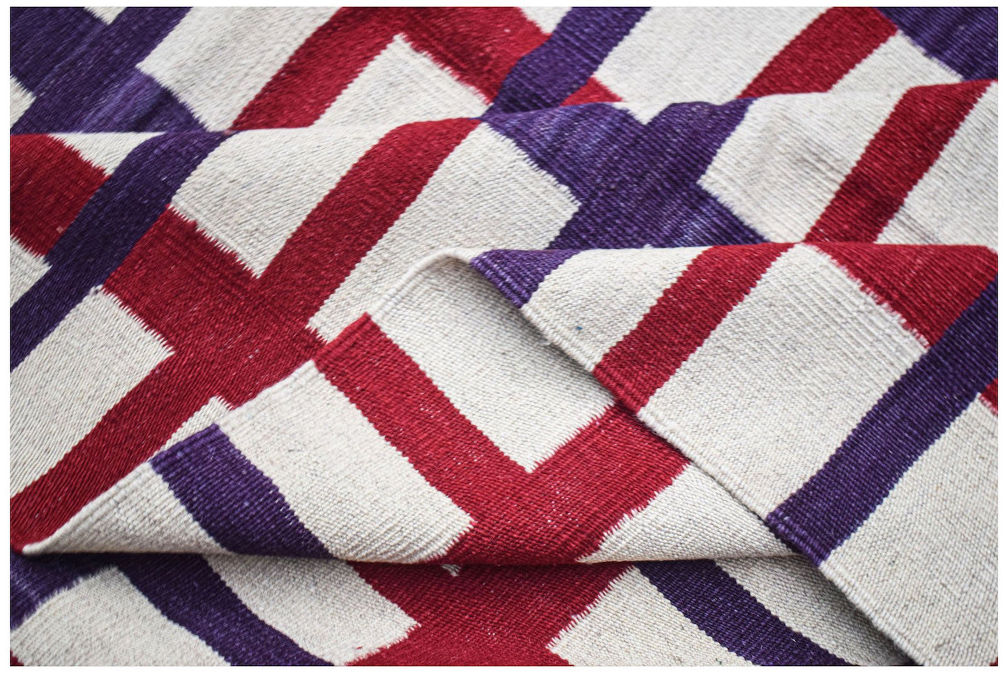 A handmade Afghan Maimana kilim rug featuring a geometric pattern in red, purple, and cream.