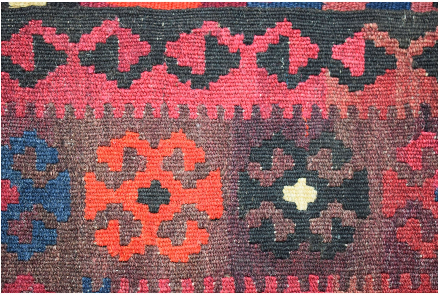 A close-up of a handmade Afghan Maimana kilim featuring geometric patterns in red, blue, and black.