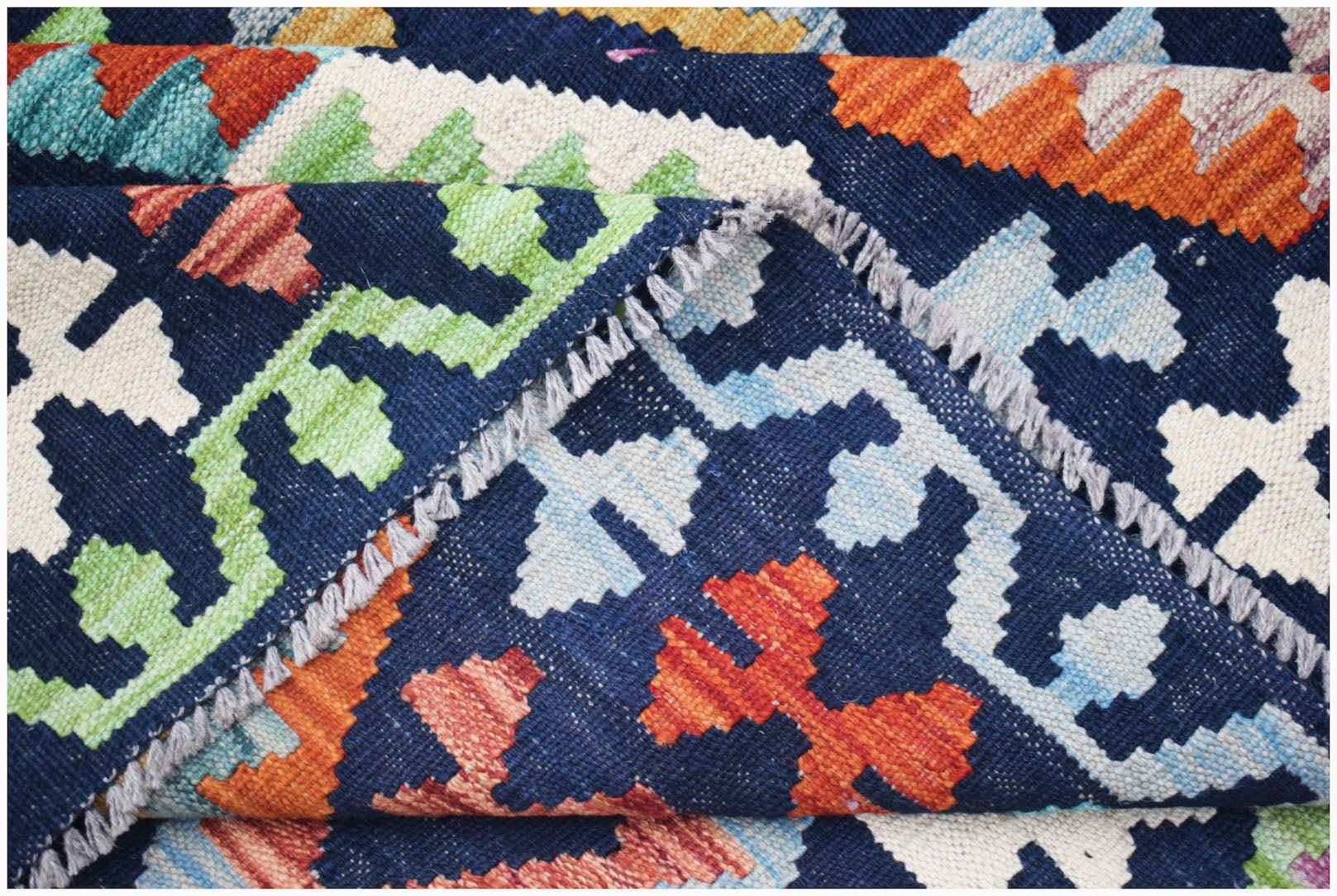 A handmade Afghan Maimana kilim rug featuring a geometric pattern in vibrant colors on a blue base.