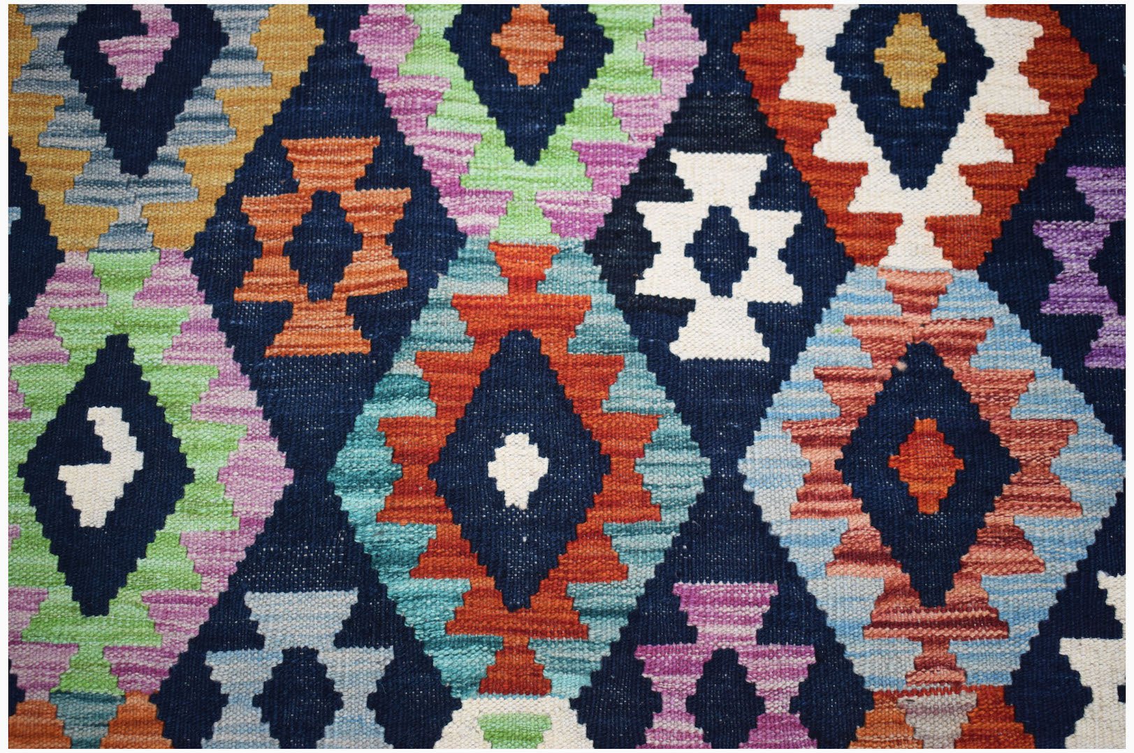 Handwoven Afghan Maimana kilim rug featuring a vibrant geometric diamond pattern on a dark background.