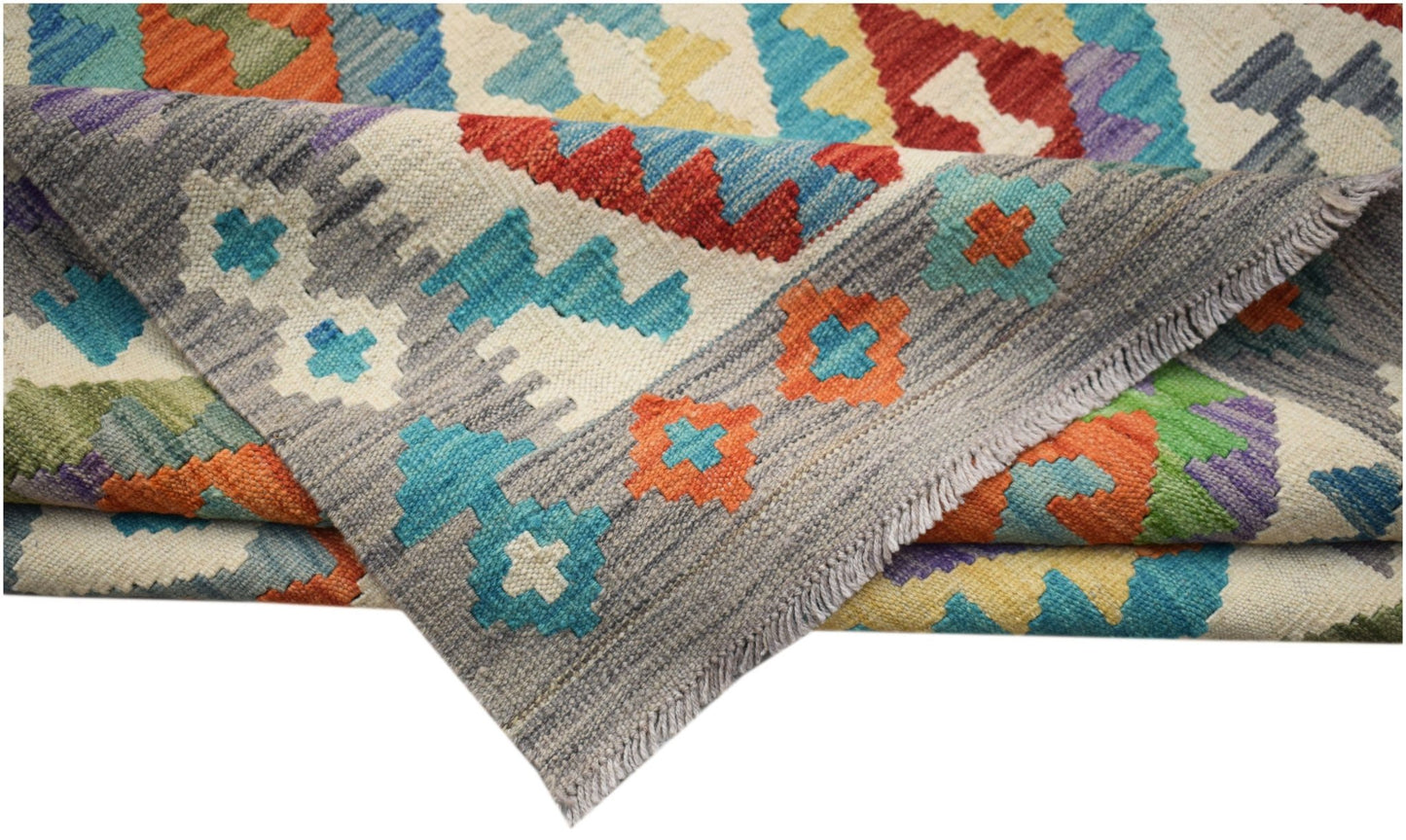 A handwoven Afghan Maimana kilim rug featuring a colorful geometric pattern on a grey background.
