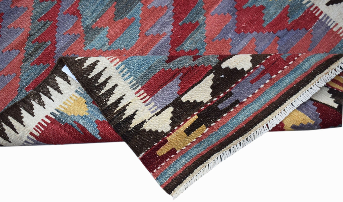 A handwoven Afghan Maimana wool kilim runner featuring geometric patterns in red, blue, and cream.