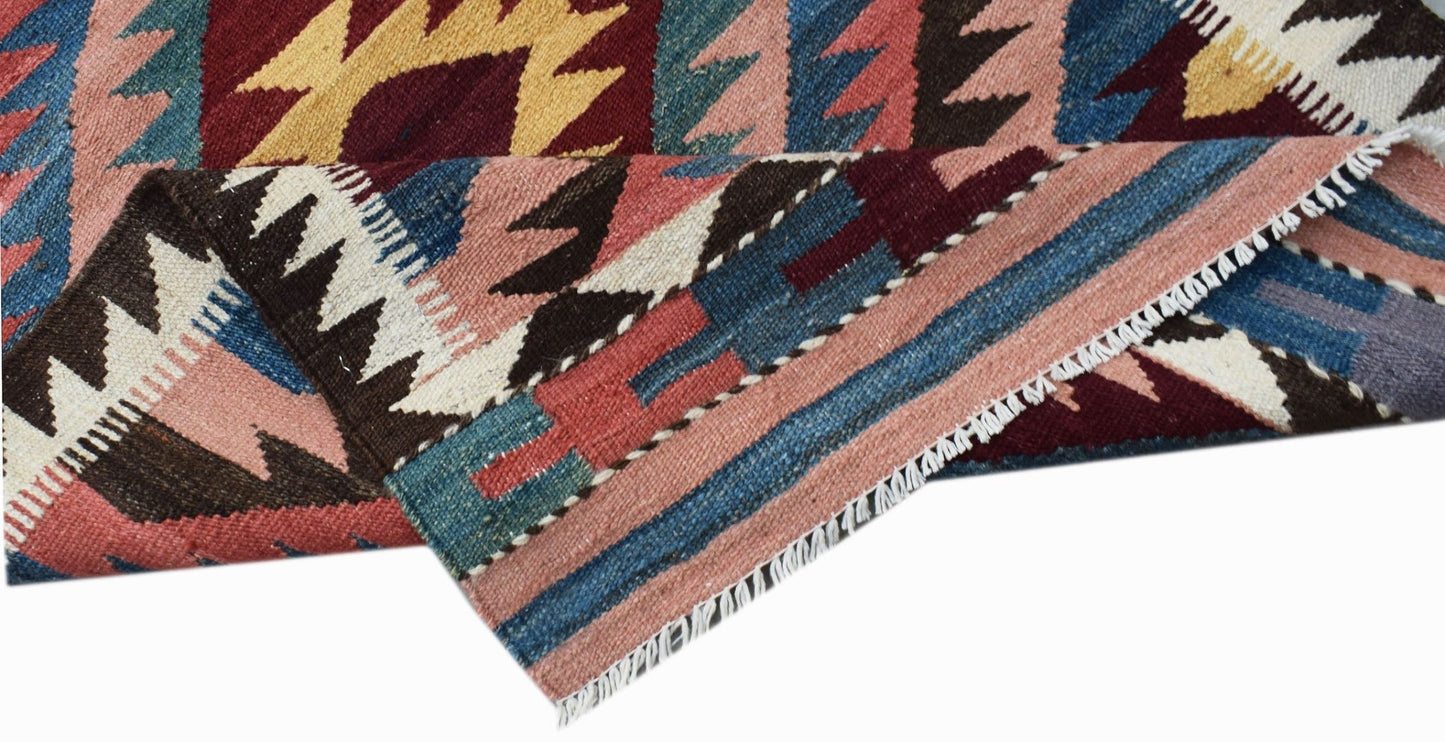 A handwoven Afghan Maimana kilim runner featuring geometric patterns in red, blue, and pink wool.