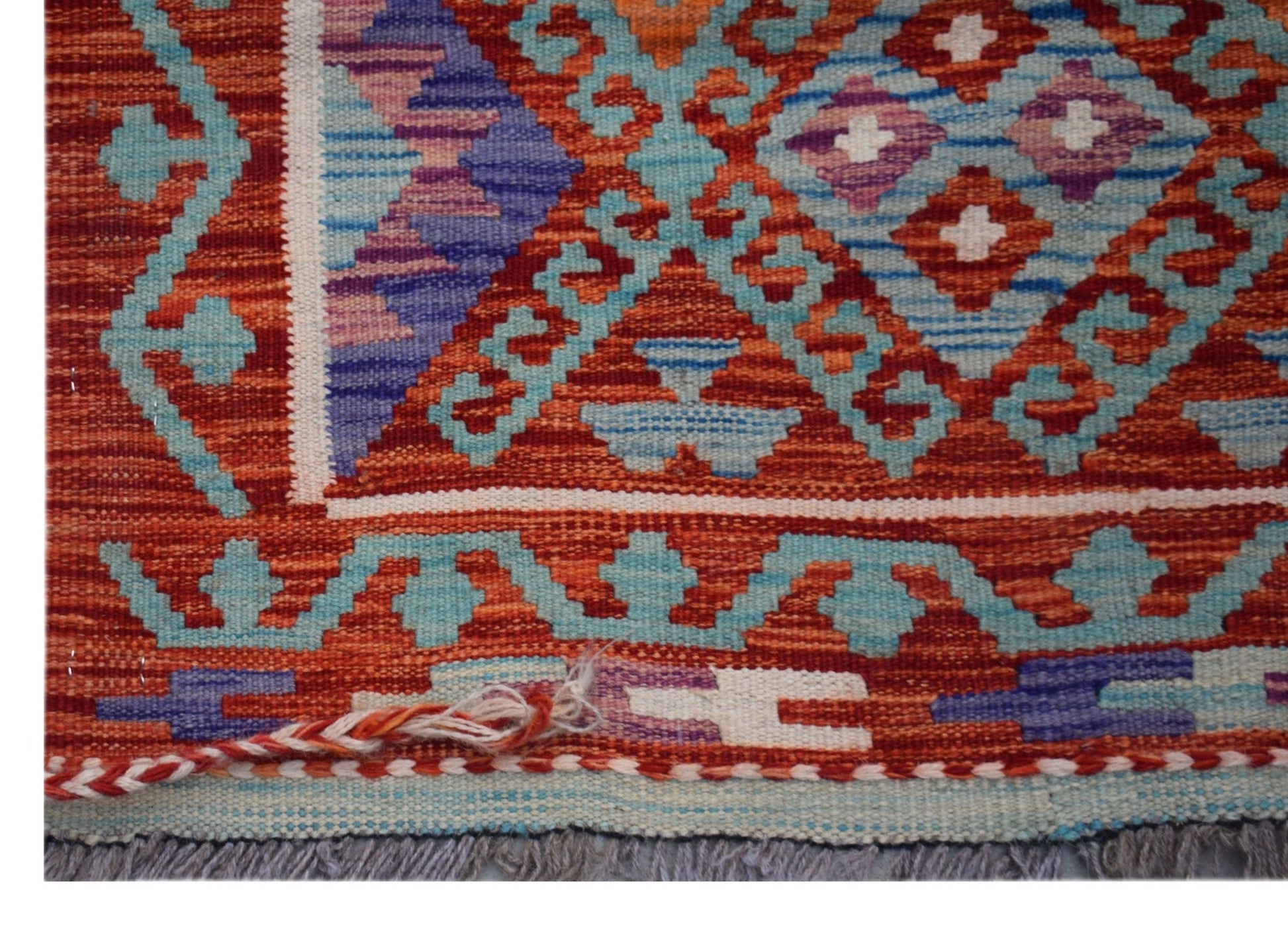 A close-up of an Afghan Maimana Kilim runner featuring geometric patterns in red, blue, and purple.
