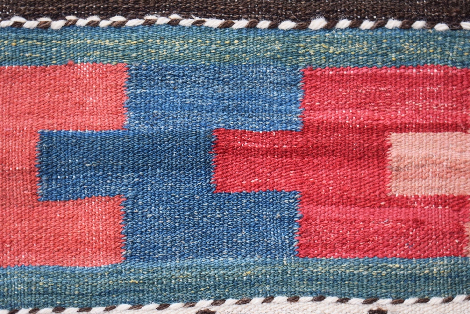 A close-up of a handmade Afghan Maimana kilim runner featuring geometric red and blue patterns.