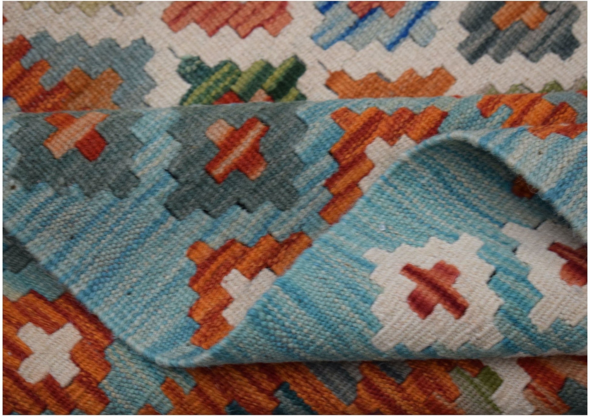 A handmade Afghan Maimana kilim rug featuring a geometric pattern in orange, blue, and cream.