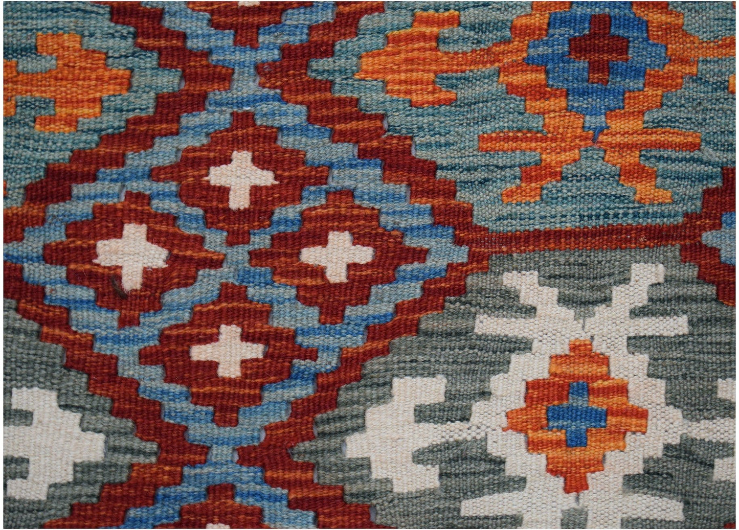 A close-up of a handmade Afghan Maimana kilim featuring geometric patterns in blue, red, and orange.
