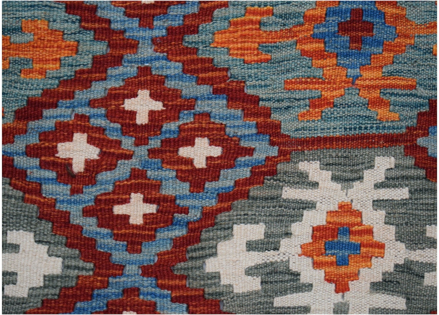 A close-up of a handmade Afghan Maimana kilim featuring geometric patterns in blue, red, and orange.