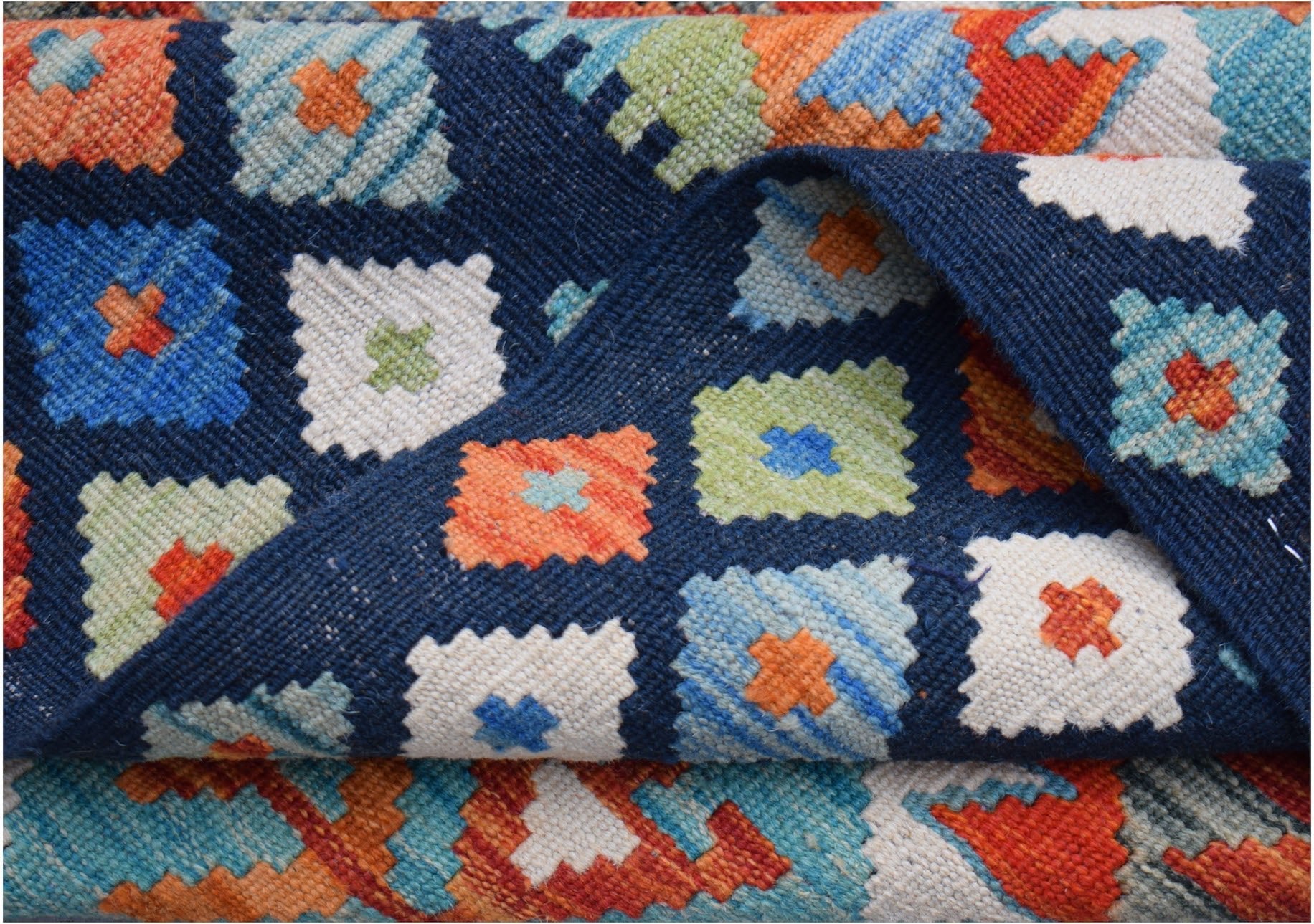 A handmade Afghan Maimana kilim rug featuring a geometric pattern of colorful squares on navy blue.