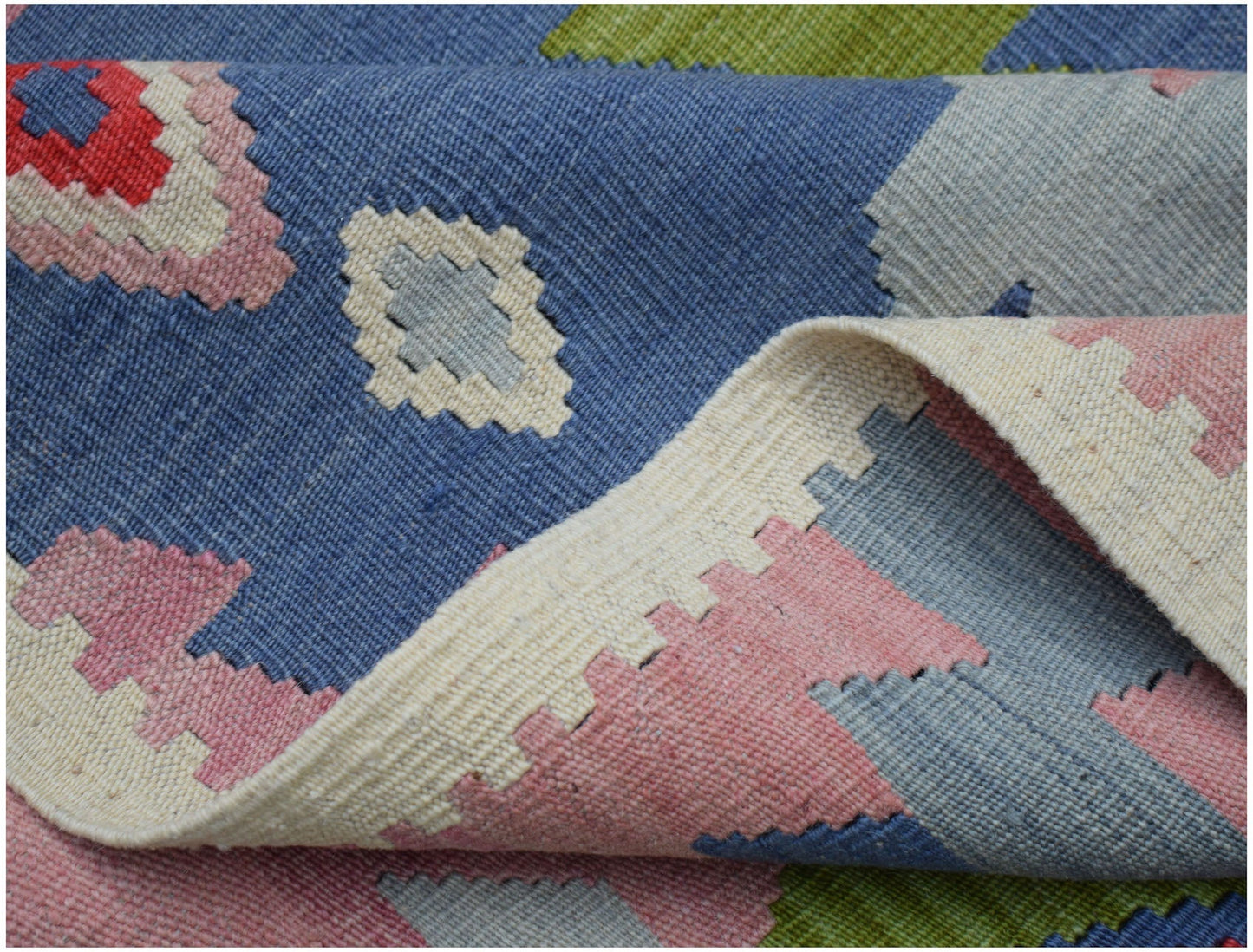 A handwoven Afghan Maimana kilim rug featuring a geometric pattern in blue, pink, and green.