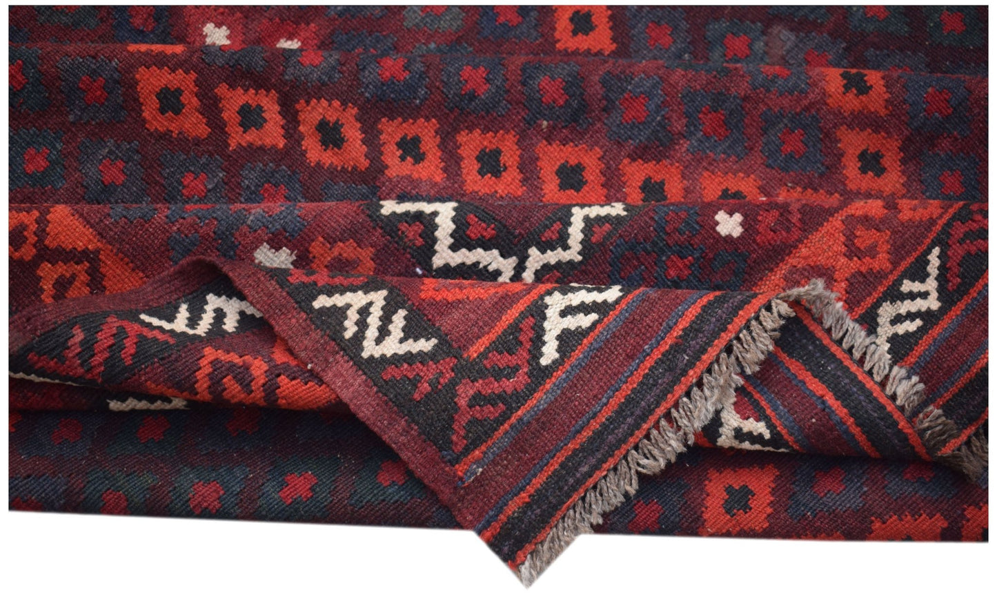 A folded Afghan Maimana kilim featuring a geometric pattern in deep red, black, and cream wool.