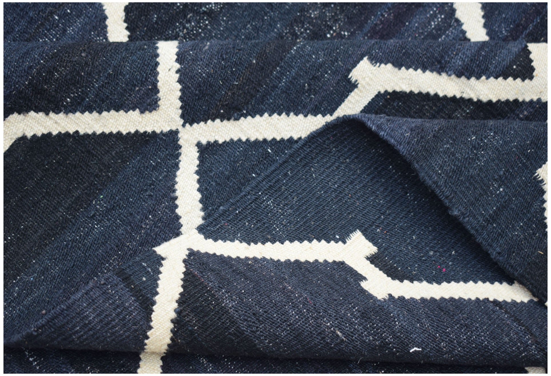 A handmade Afghan Maimana kilim rug featuring a dark blue field with a white geometric pattern.