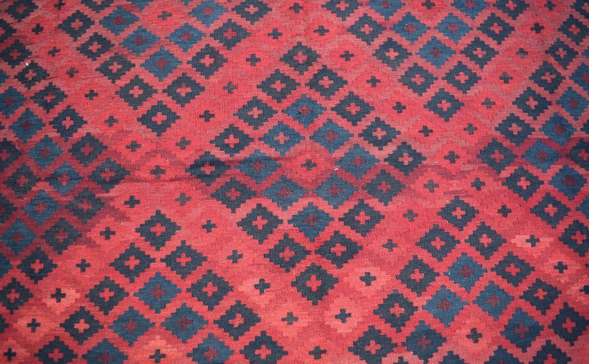 Handwoven Afghan Maimana kilim featuring a repeating geometric pattern in red and dark blue wool.