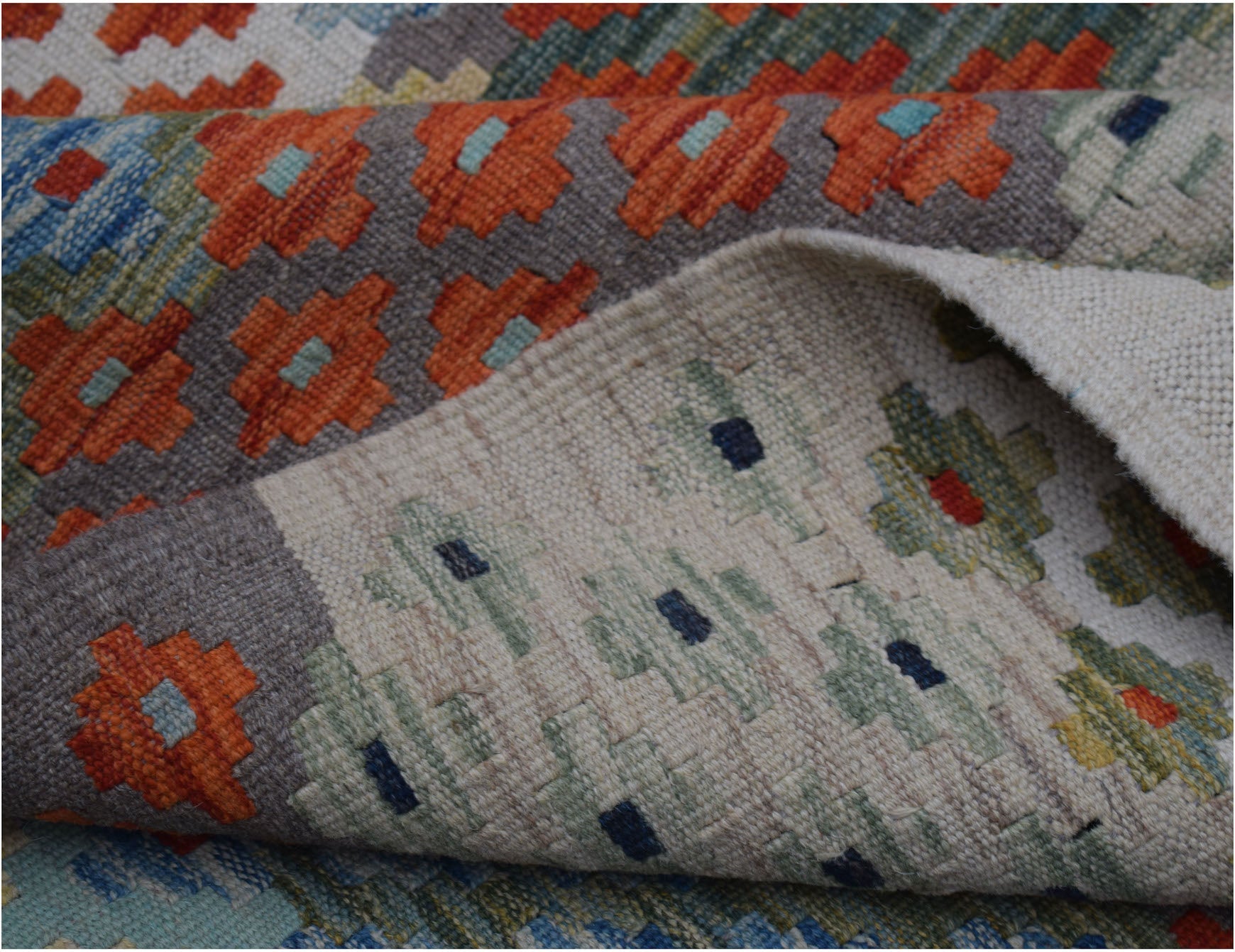 A handwoven Afghan Maimana kilim rug featuring geometric patterns in orange, blue, and green.