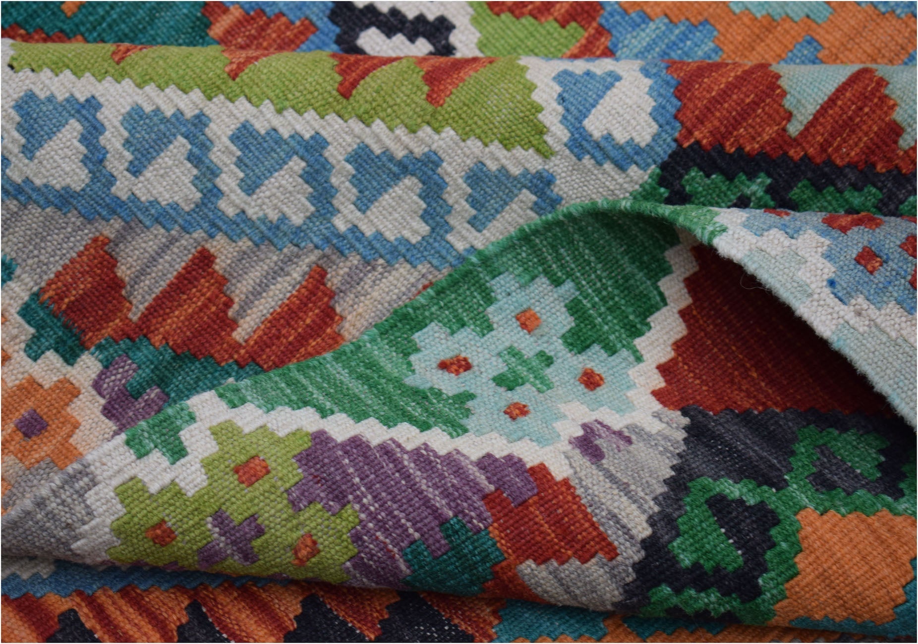 A handmade Afghan Maimana kilim rug featuring a vibrant, geometric pattern in wool.