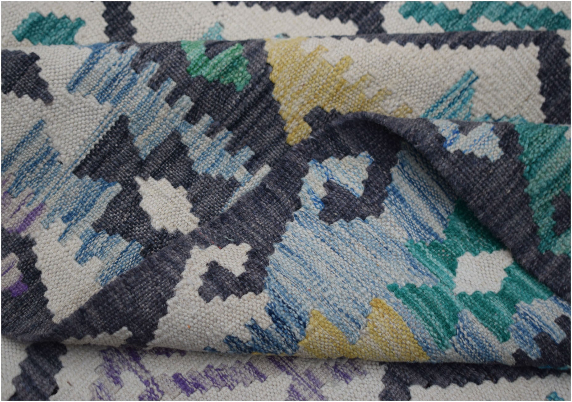 A handwoven Afghan Maimana kilim rug featuring a geometric pattern in blue, green, and yellow.