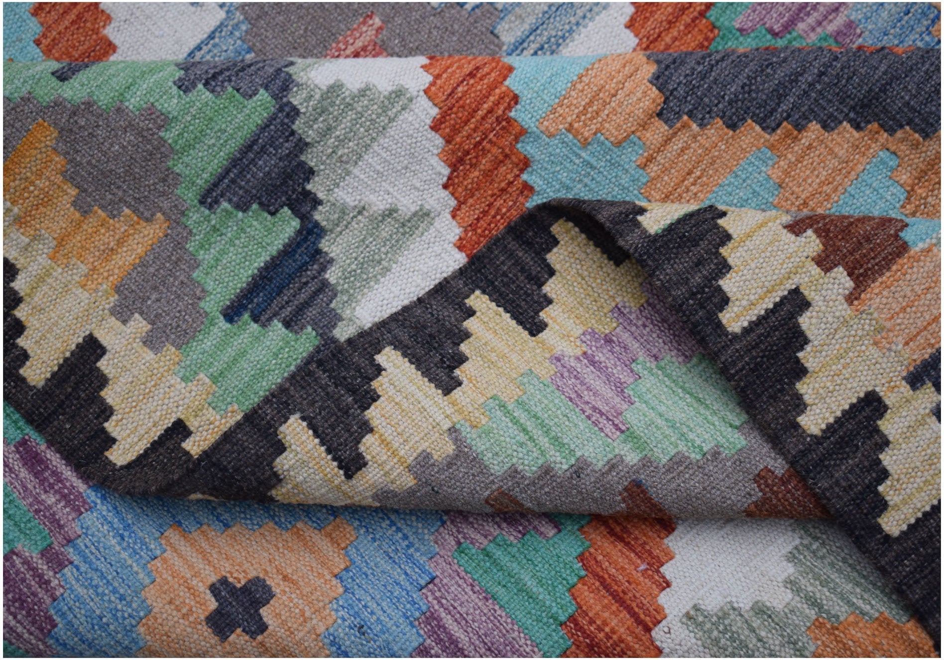 A handmade Afghan Maimana kilim rug featuring a vibrant, geometric pattern in wool.