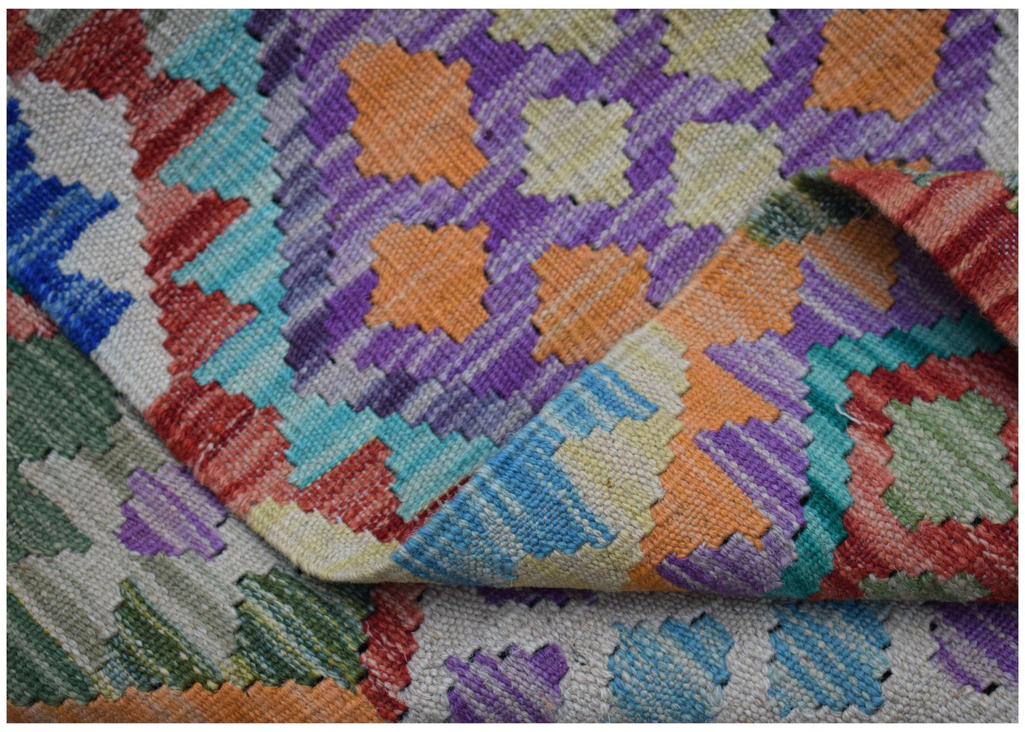 A handwoven Afghan Maimana kilim rug featuring a vibrant, geometric pattern in wool.