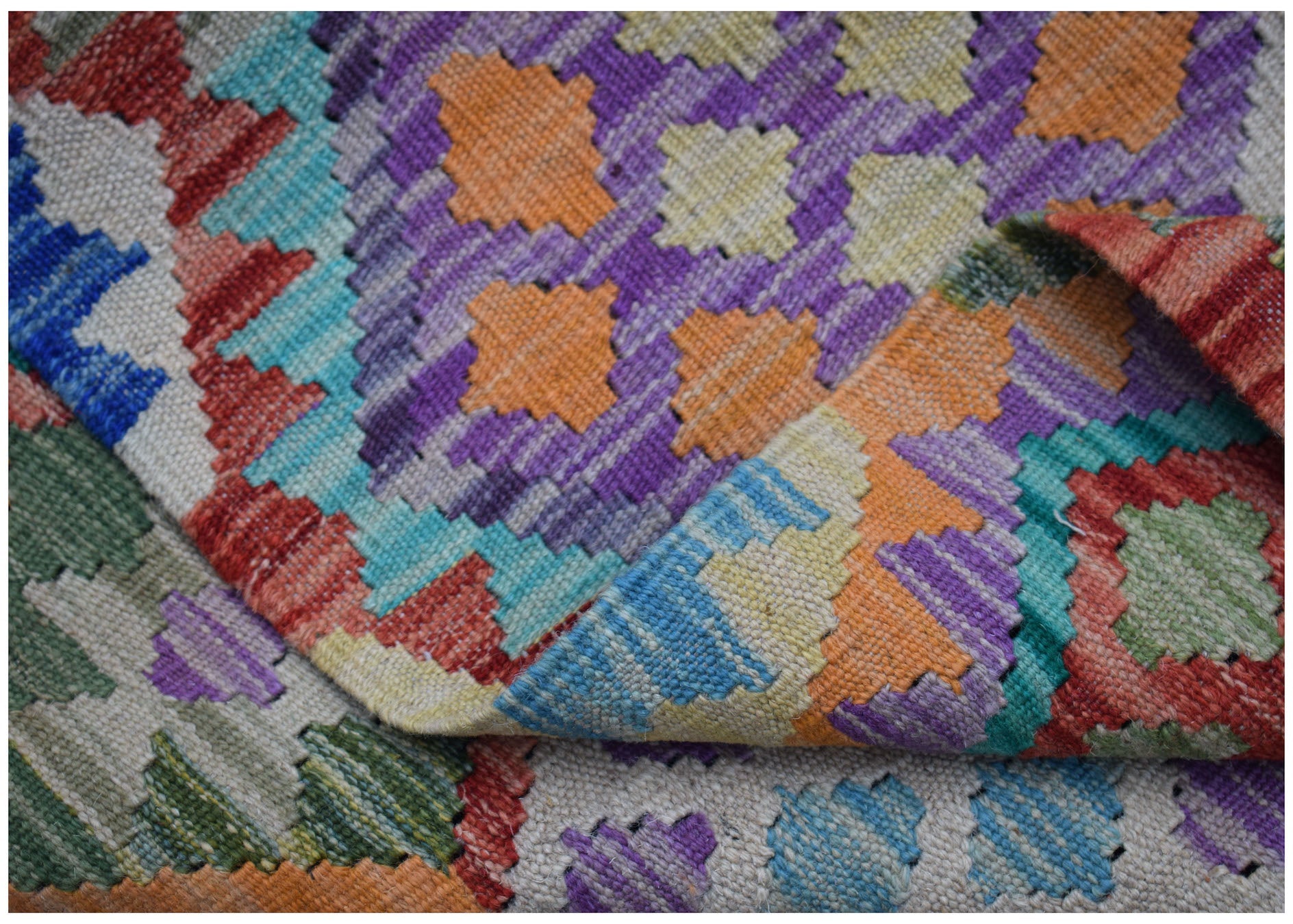 A handwoven Afghan Maimana kilim rug featuring a vibrant, geometric pattern in wool.