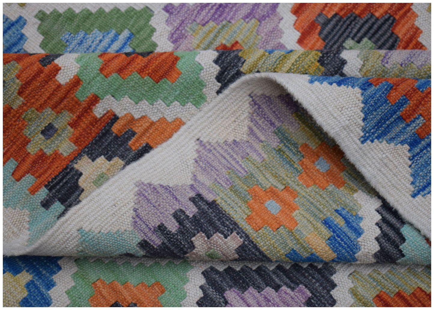 A handwoven Afghan Maimana kilim rug featuring a colorful geometric pattern on a flatweave wool.