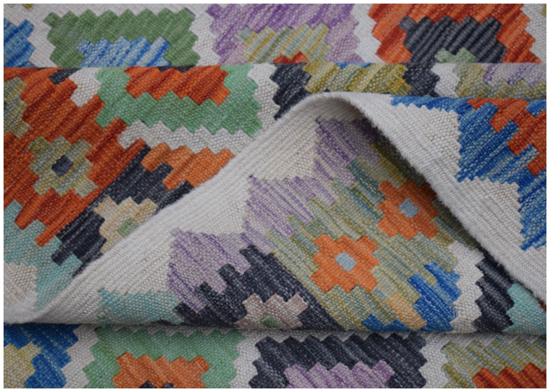 A handwoven Afghan Maimana kilim rug featuring a colorful geometric pattern on a flatweave wool.