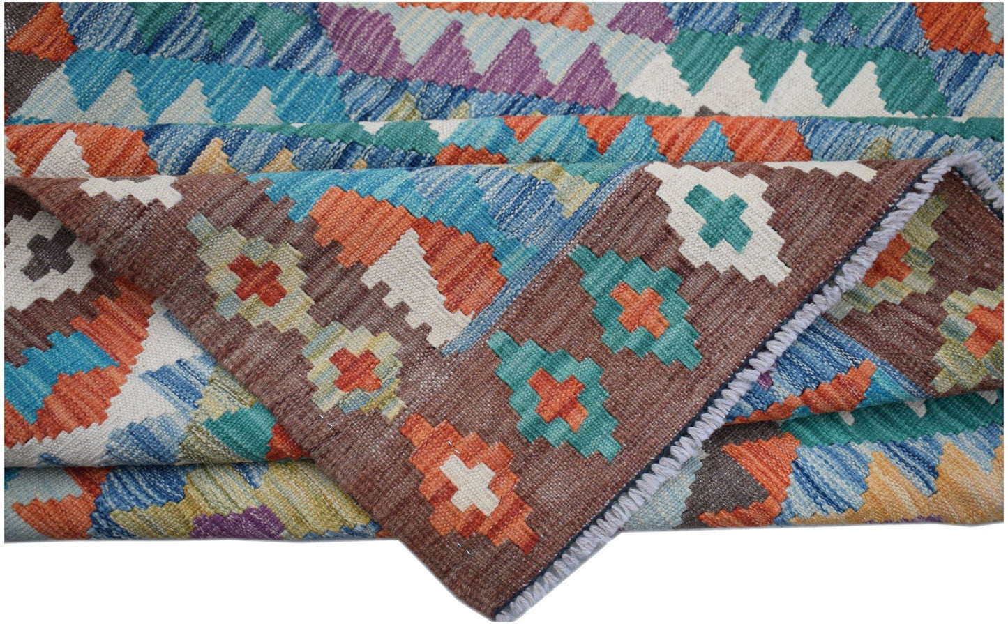 A handmade Afghan Maimana kilim rug featuring a colorful geometric pattern on a brown background.