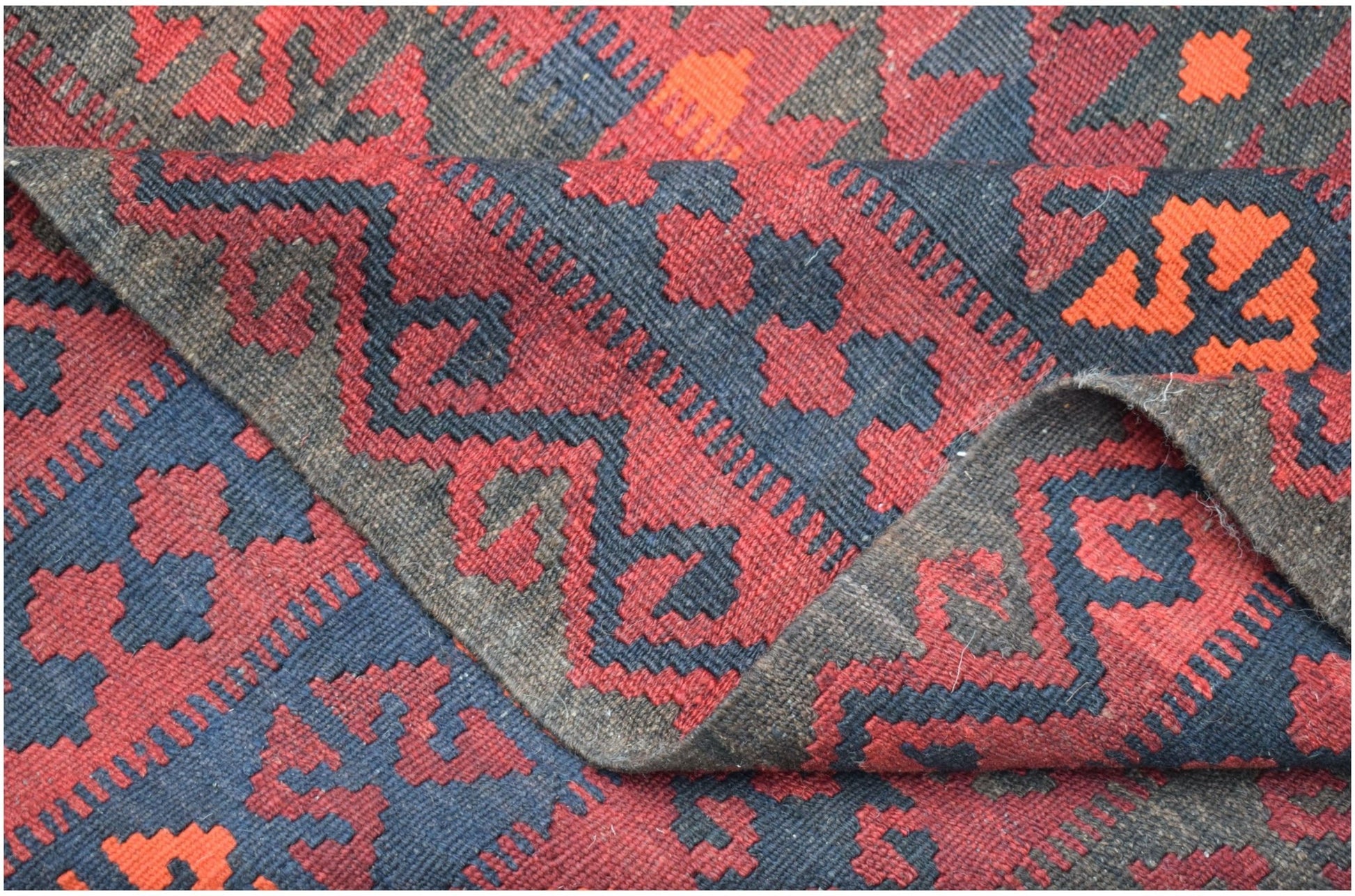A handwoven Afghan Maimana kilim rug featuring a geometric pattern in red, black, and orange wool.