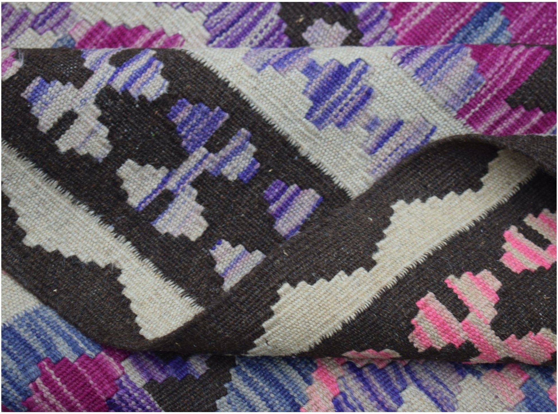 A handwoven Afghan Maimana kilim rug featuring a geometric pattern in purple, pink, and dark brown.