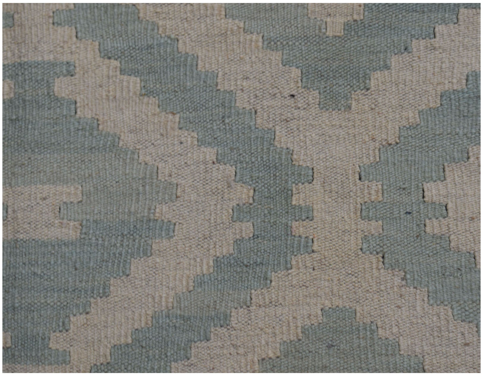 A handmade Afghan Maimana kilim rug featuring a geometric pattern in sage green and cream wool.