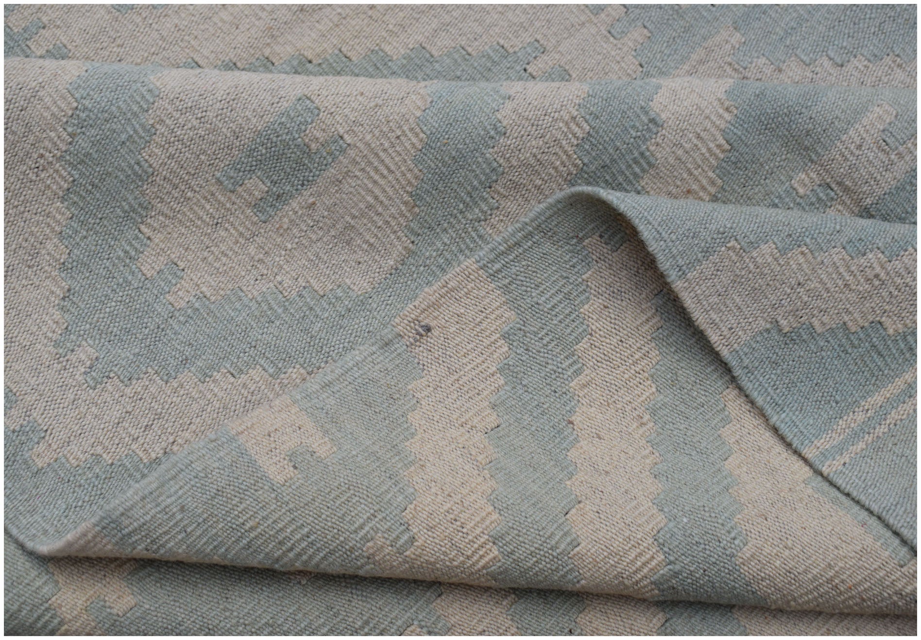 A handwoven Afghan Maimana kilim rug featuring a geometric pattern in light blue and cream wool.