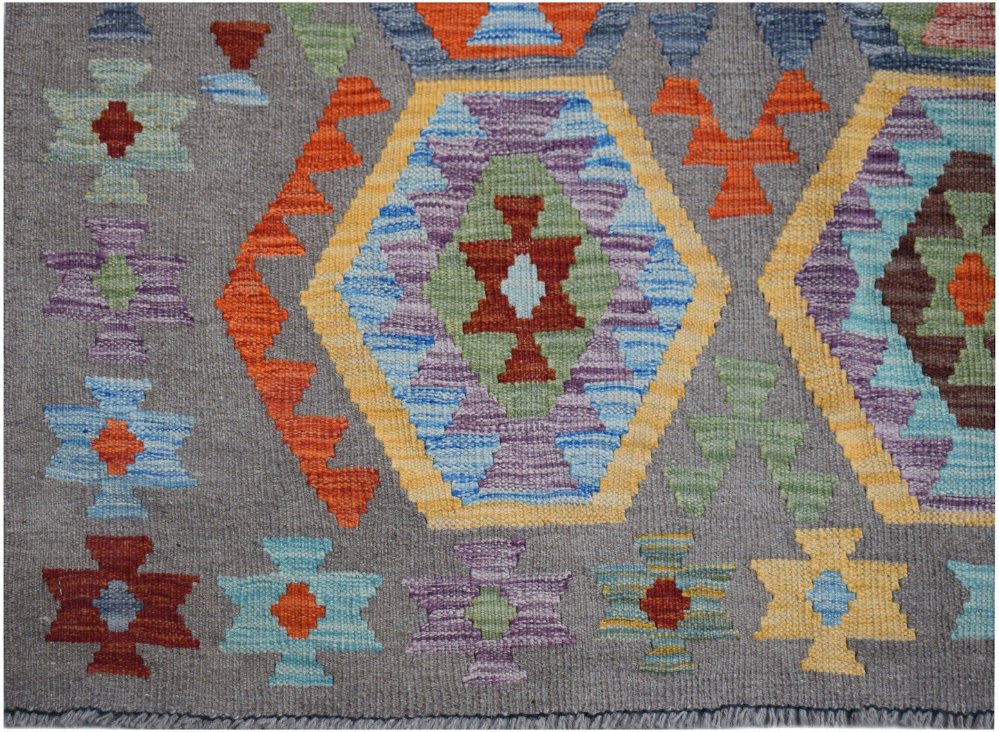 Handwoven Afghan Maimana kilim rug featuring colorful geometric patterns on a gray wool background.