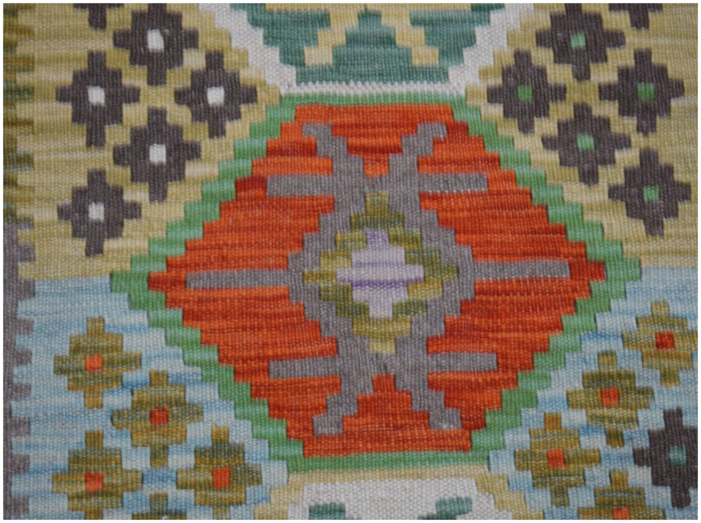 A handmade Afghan Maimana kilim runner featuring a geometric pattern in orange, green, and grey.