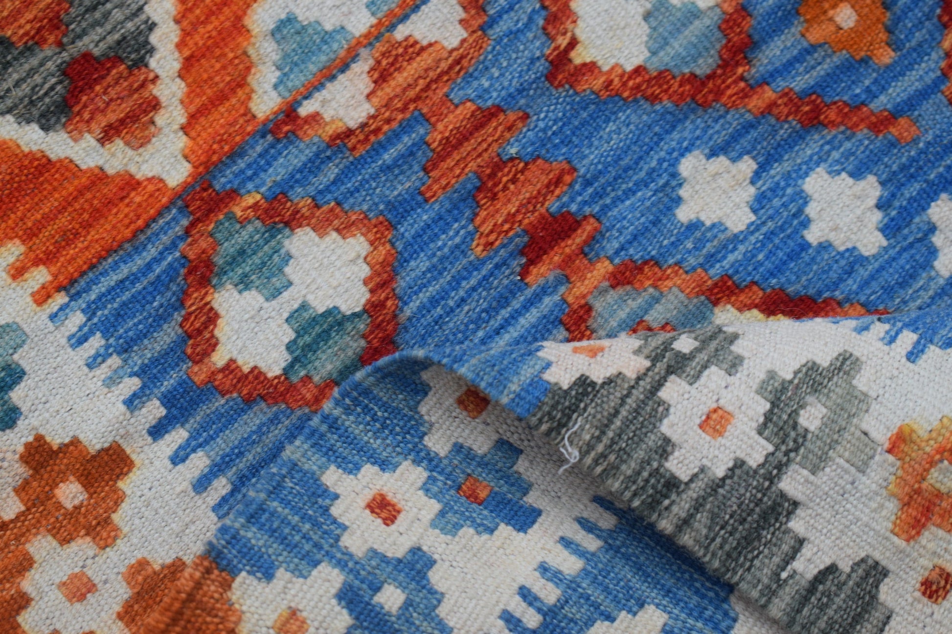 A handmade Afghan Maimana kilim runner featuring a geometric pattern in blue, orange, and white.