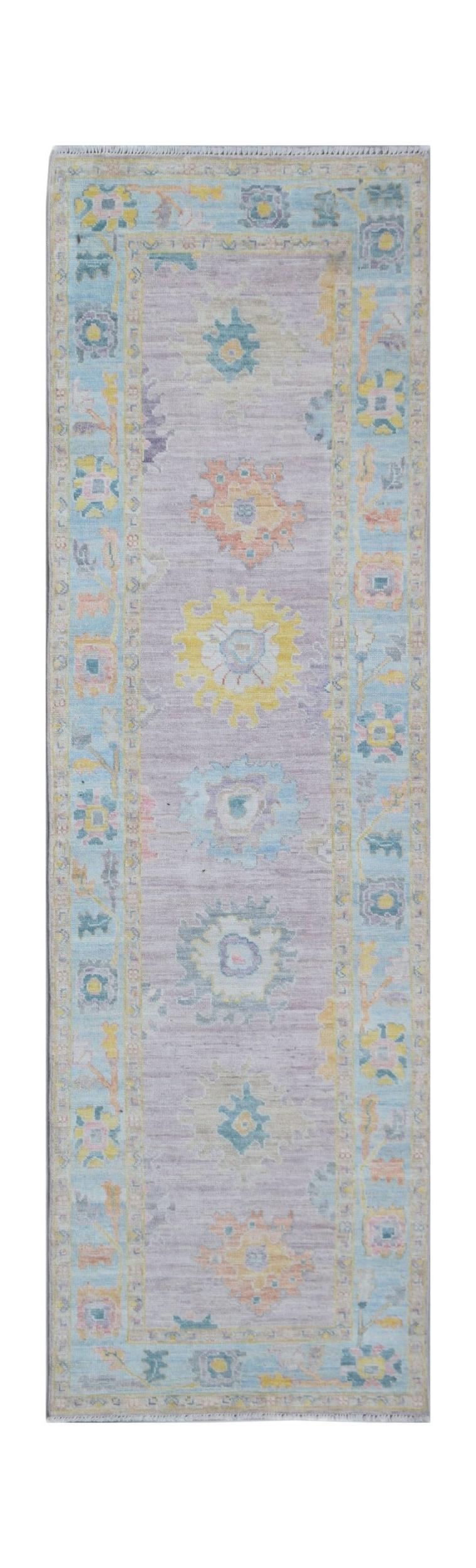 A handmade wool runner rug featuring a light purple field with colorful floral motifs and borders.