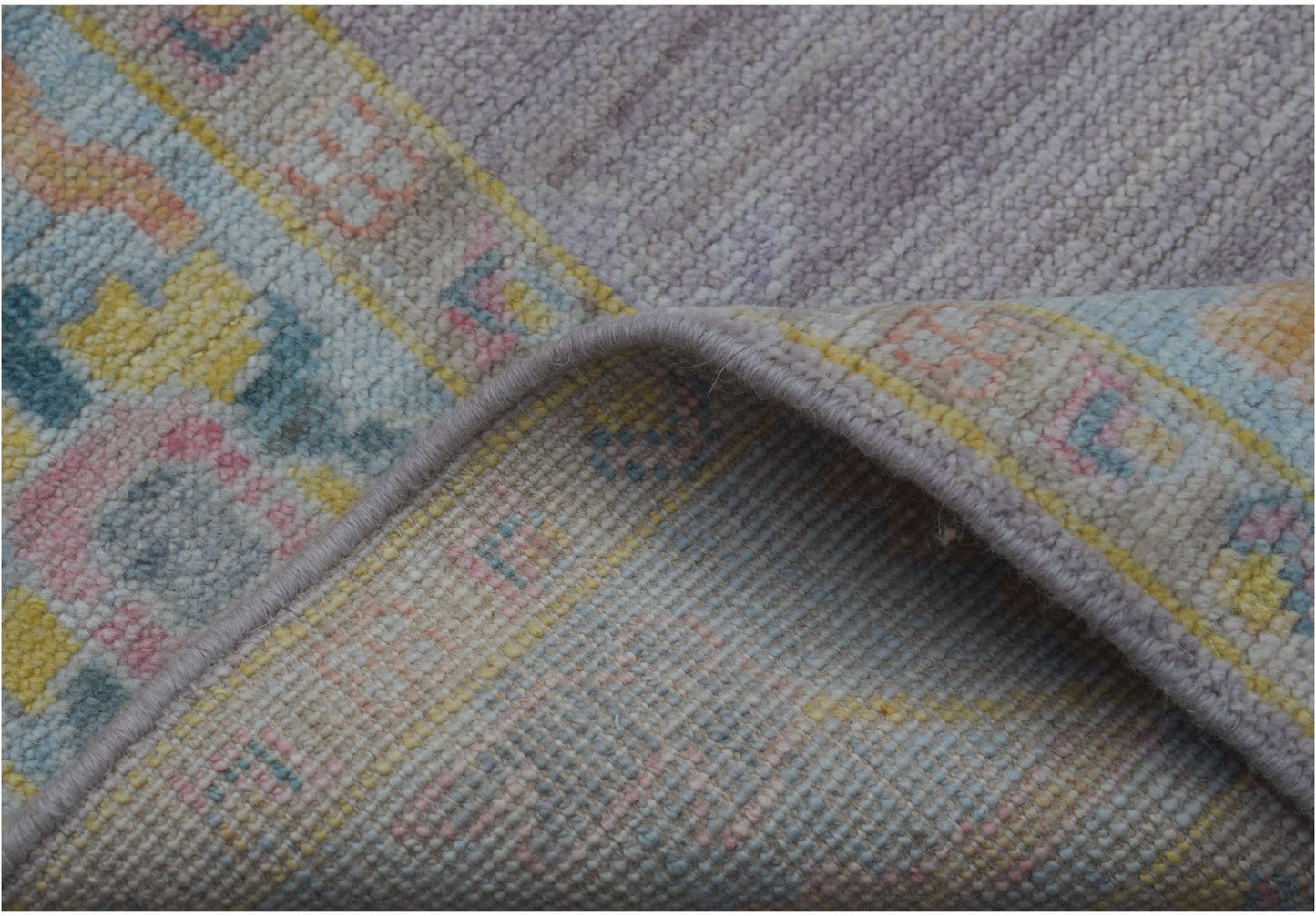 A folded handmade wool runner rug featuring a traditional pattern in soft pastel tones.