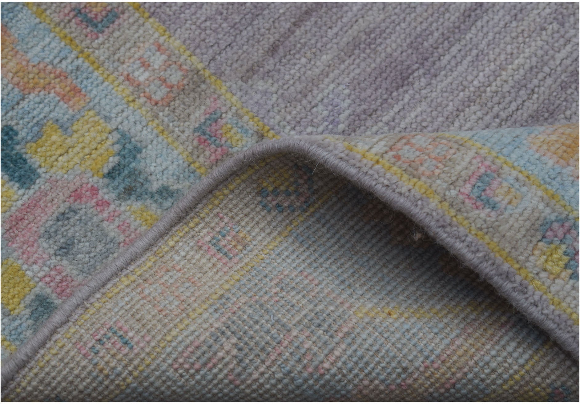 A folded handmade wool runner rug featuring a traditional pattern in soft pastel tones.