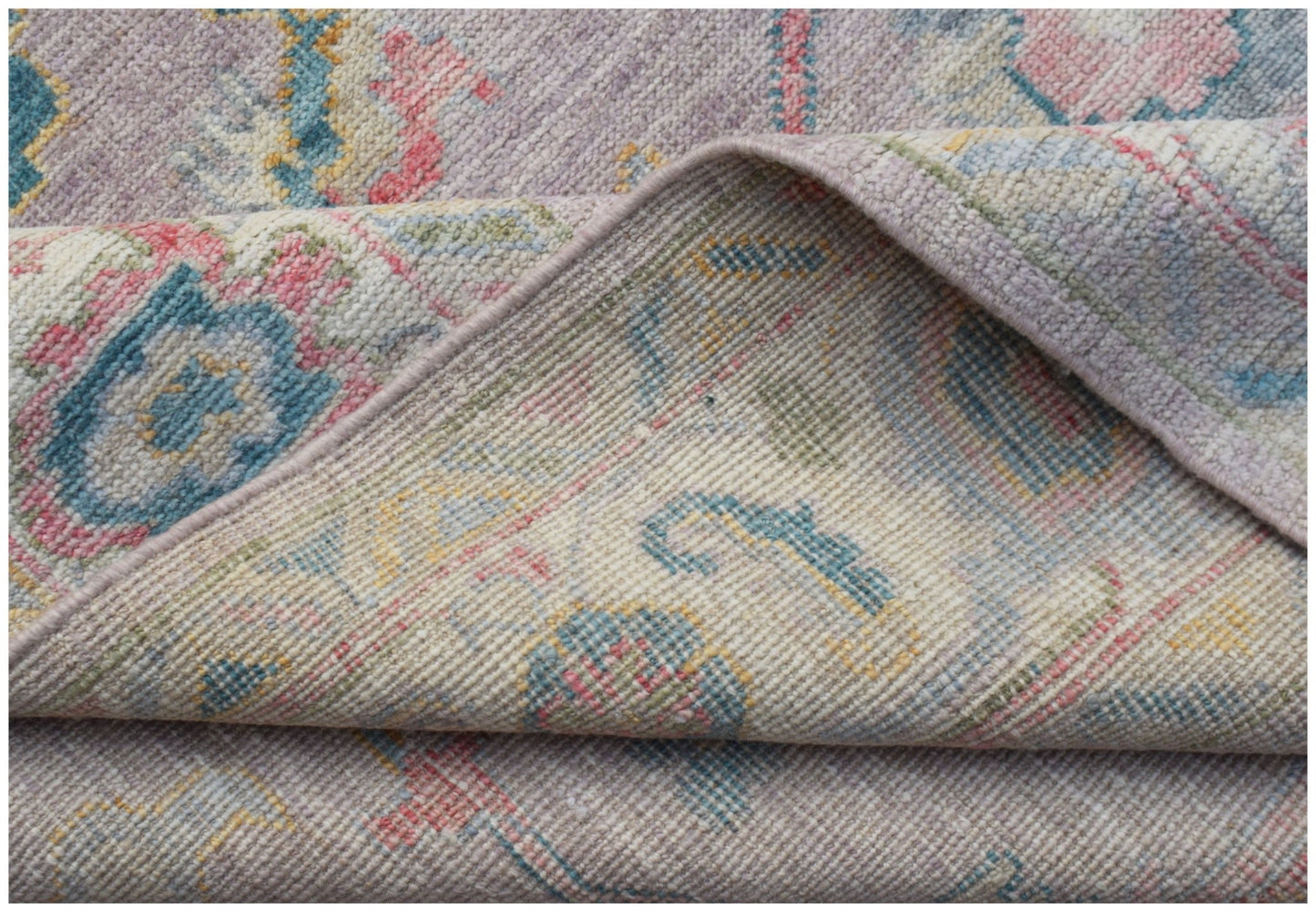 A folded transitional Oushak rug featuring a traditional floral pattern in soft pastel tones.